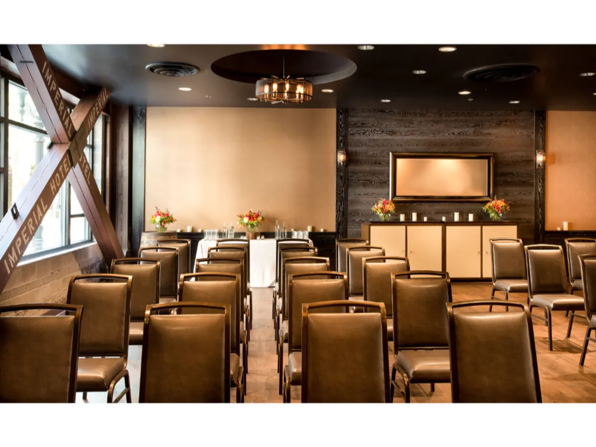 A refined interior space featuring rows of seating, elegant floral arrangements, and a designated presentation area. The clean lines and formal yet welcoming atmosphere evoke the feel of a modern business lounge or meeting venue.