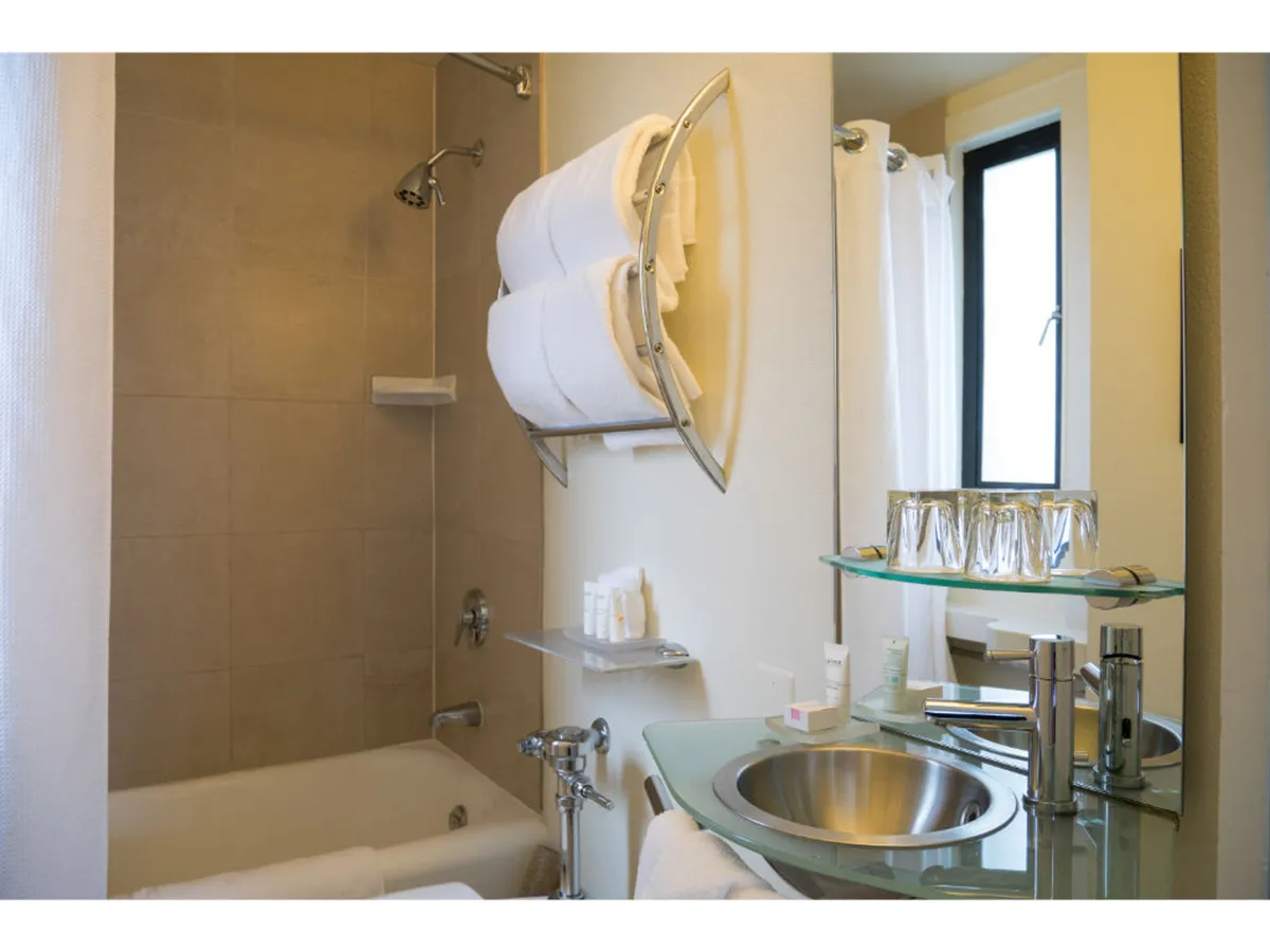 A bright, modern bathroom featuring a sleek bathtub, sink, fresh towels, and a window allowing in natural light. The clean lines and soothing palette create an atmosphere of refreshment and tranquility.